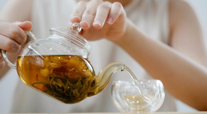 Žena drži providni čajnik sa prirodnim čajem i sipa u providnu šoljicu.