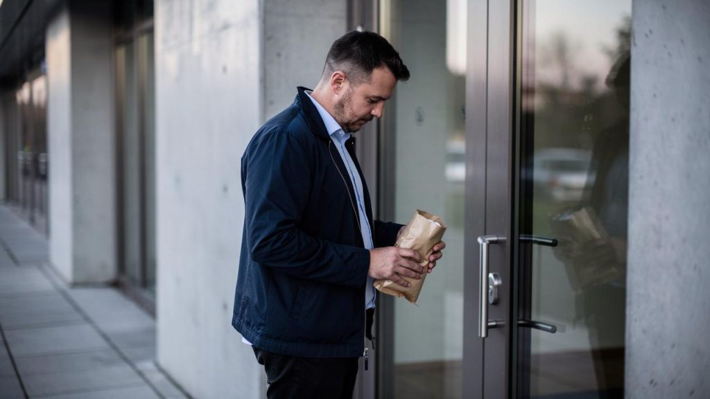 Muškarac drži smeđi papirni paket ispred staklenih vrata