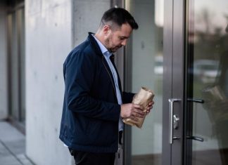Emocionalno prejedanje: kako prepoznati okidače? Muškarac drži smeđi papirni paket ispred staklenih vrata
