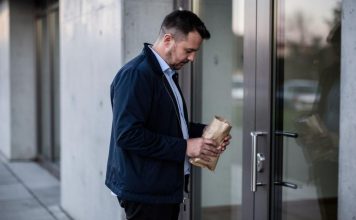 Emocionalno prejedanje: kako prepoznati okidače? Muškarac drži smeđi papirni paket ispred staklenih vrata