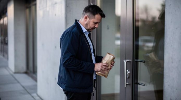Muškarac drži smeđi papirni paket ispred staklenih vrata