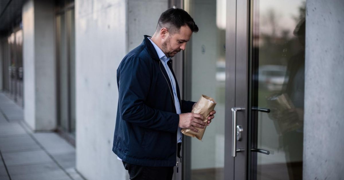 Muškarac drži smeđi papirni paket ispred staklenih vrata