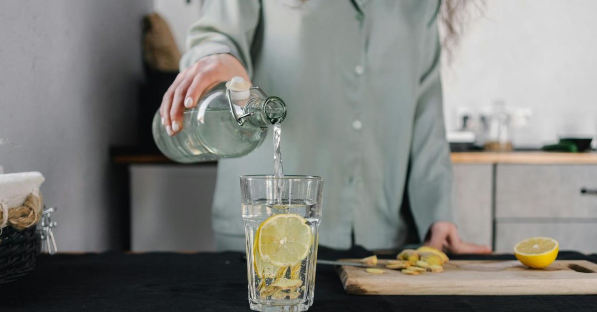 osoba-casa-kuhinja-limun-voda Osoba sipa vodu u staklenu čašu u kuhinji.