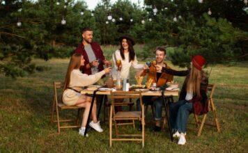 Društvo mladih nazdravlja i sedi za drvenim stolom u prirodi