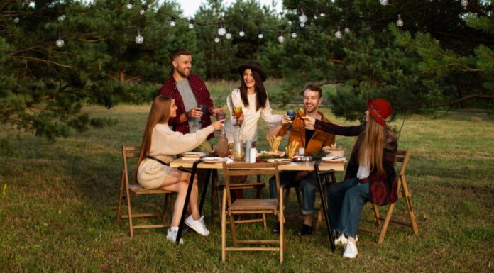 Društvo mladih nazdravlja i sedi za drvenim stolom u prirodi