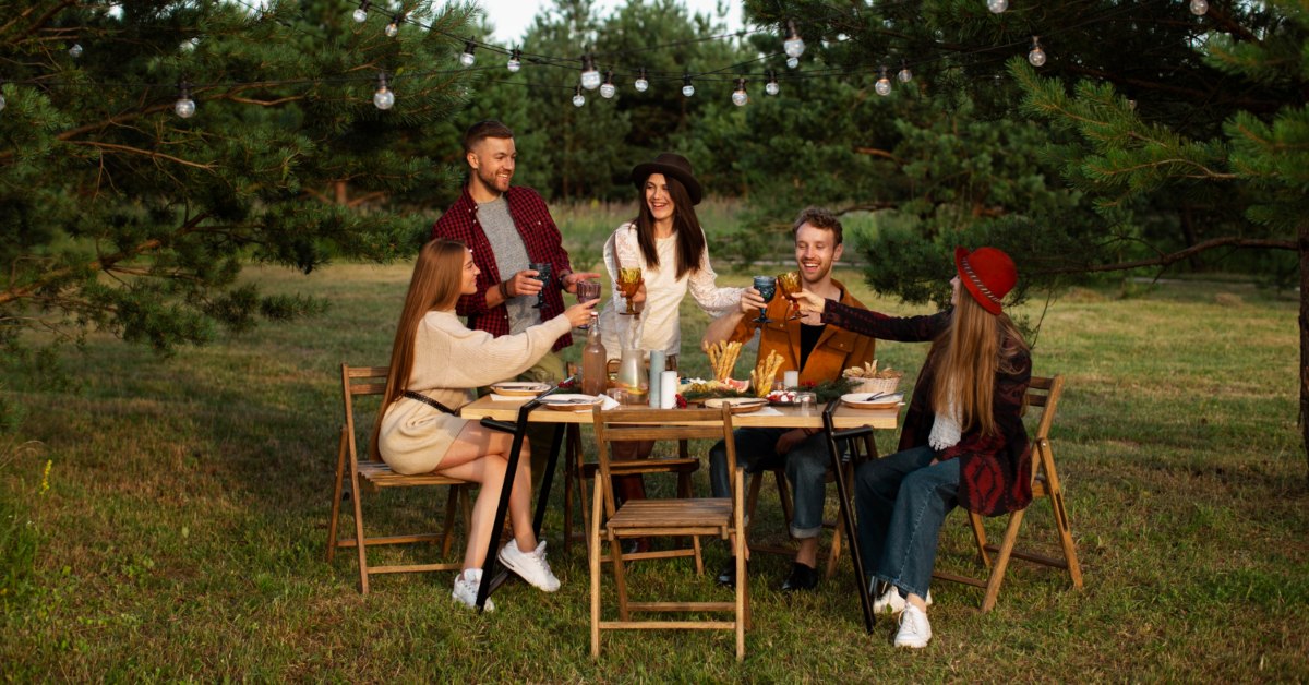 Društvo mladih nazdravlja i sedi za drvenim stolom u prirodi