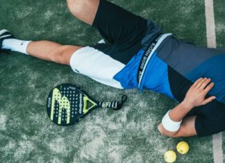 Čovek leži na travi, pored njega su reket i loptice.