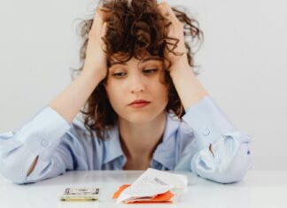 Devojka se drži za glavu dok gleda u novac i račune