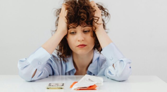 Devojka se drži za glavu dok gleda u novac i račune