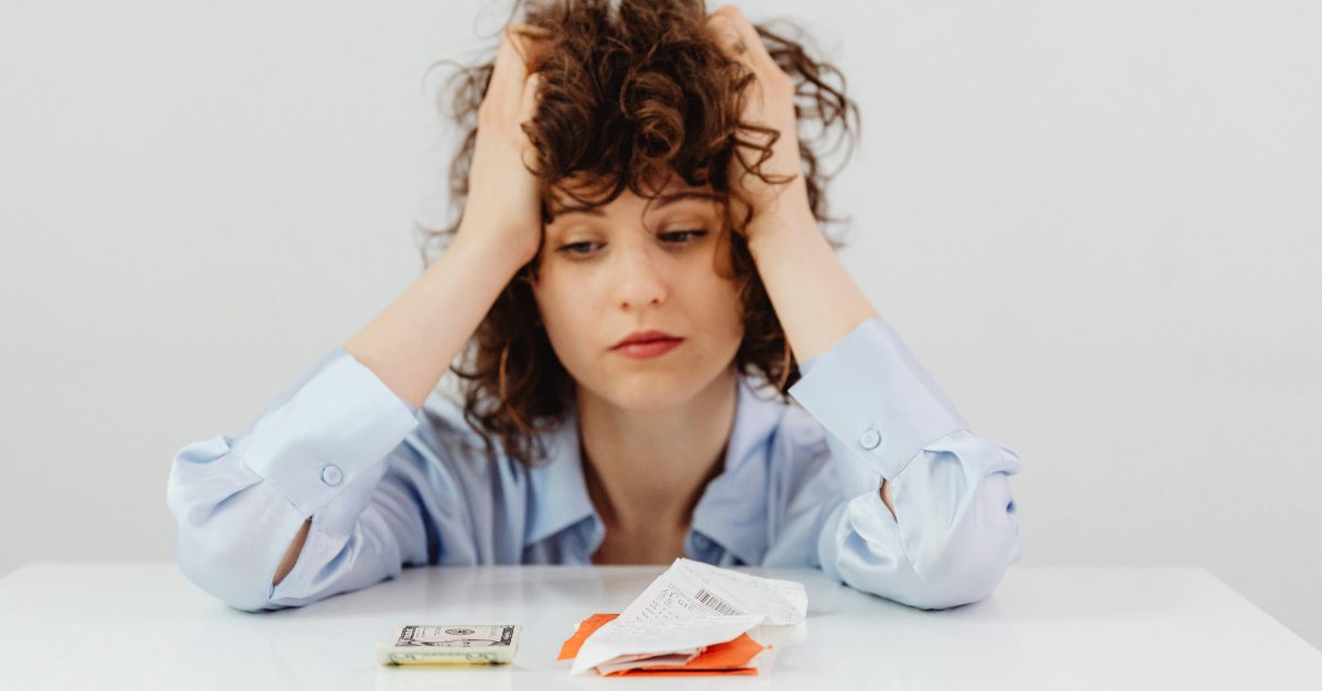 Devojka se drži za glavu dok gleda u novac i račune