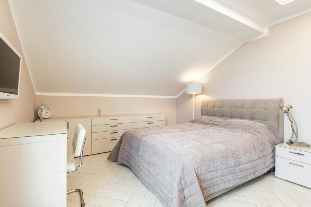 Spavaća soba sa tapaciranim krevetom ispod kosog plafona