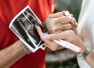 Muškarac drži za ruku ženu koja drži sliku ultrazvuka i test na trudnoću