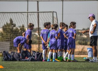 Trener razgovara sa decom u ljubičastim dresovima na fudbalskom terenu