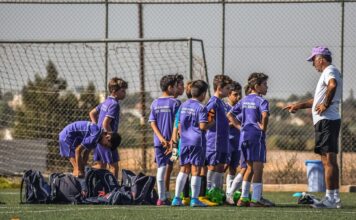 Trener razgovara sa decom u ljubičastim dresovima na fudbalskom terenu