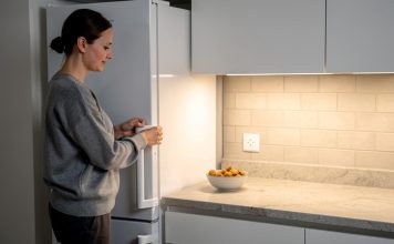 Žena otvara frižider u kuhinji dok na radnoj površini stoji činija sa grickalicama