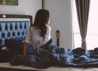 Žena sedi na krevetu i gleda kroz prozor