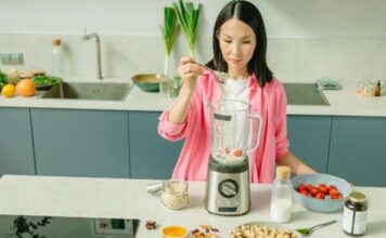 Kako organska ishrana poboljšava energiju i koncentraciju? Žena u roze košulji dodaje ovsene pahuljice u blender na kuhinjskom pultu.