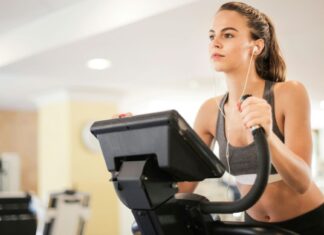 Žena na sobnom biciklu u teretani sa slušalicama