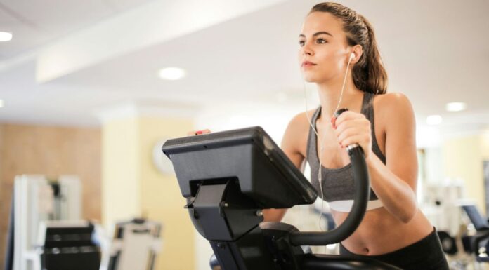 Žena na sobnom biciklu u teretani sa slušalicama