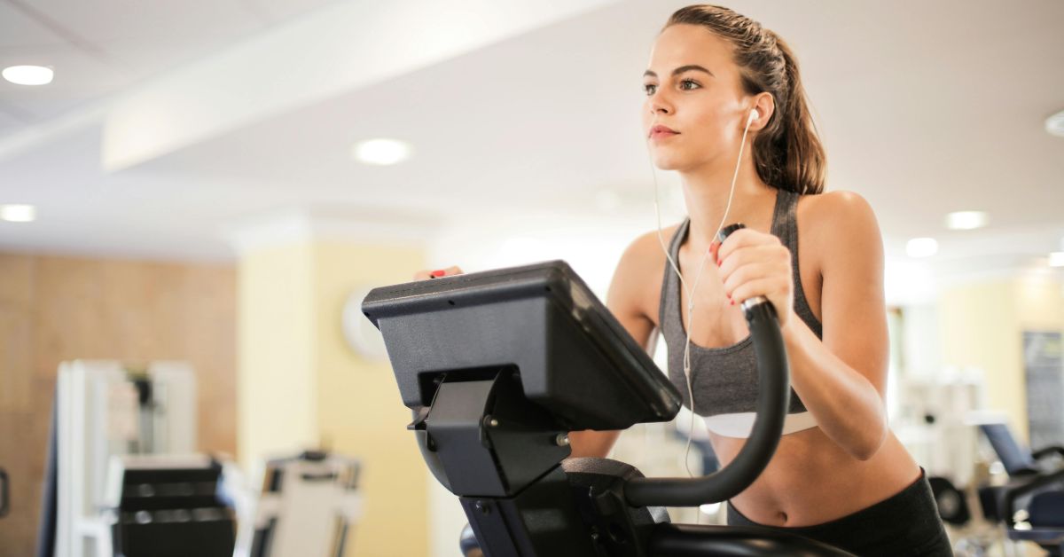 Žena na sobnom biciklu u teretani sa slušalicama